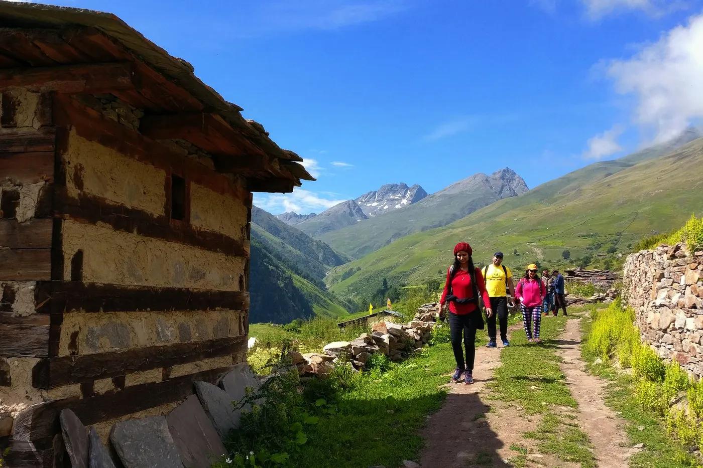 Group of hikers walking along a trail in a beautiful mountain landscape with an old hut nearby.