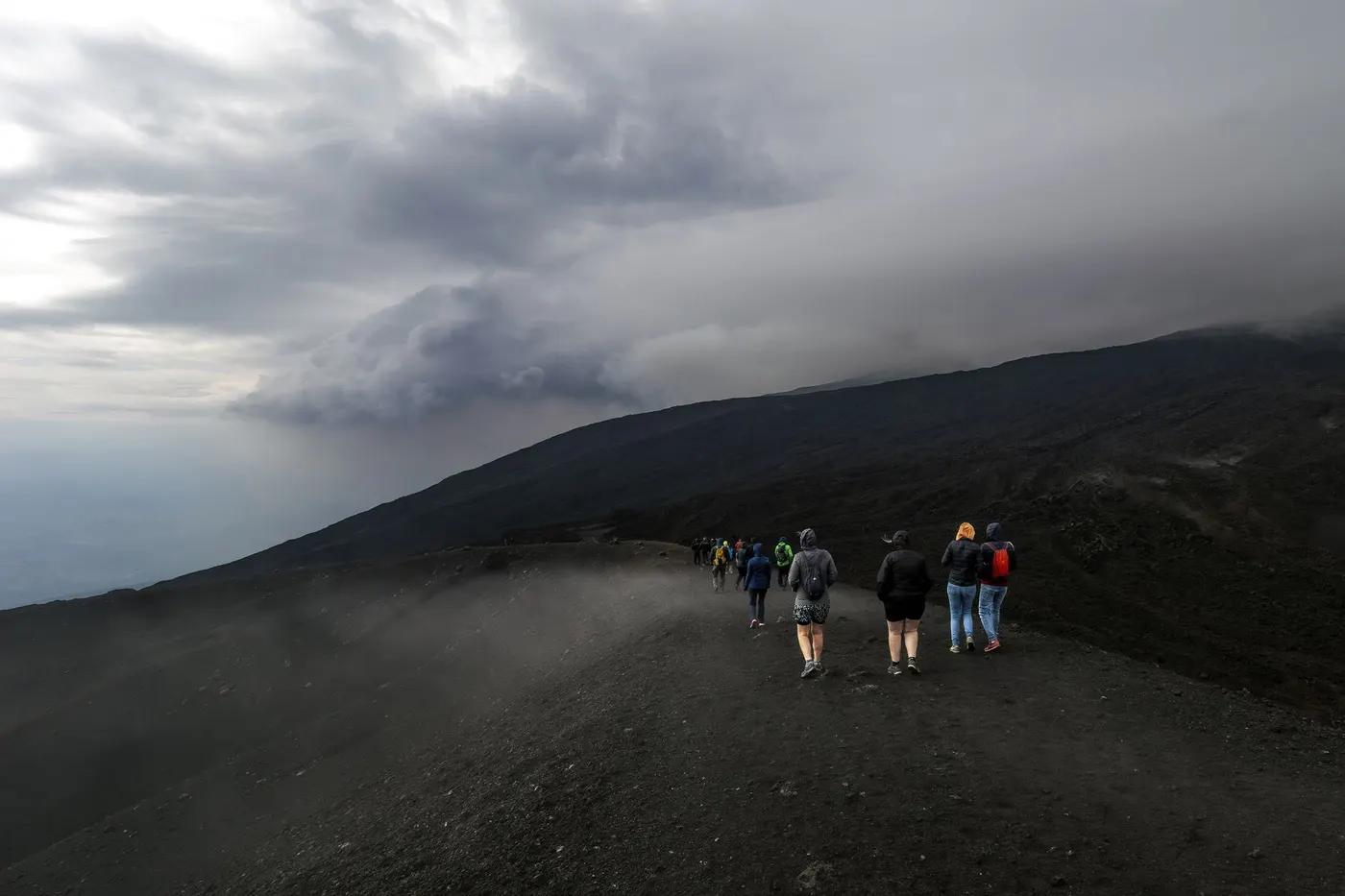 Group of people hiking on a volcanic landscape under a dramatic cloudy sky, creating a moody atmosphere.