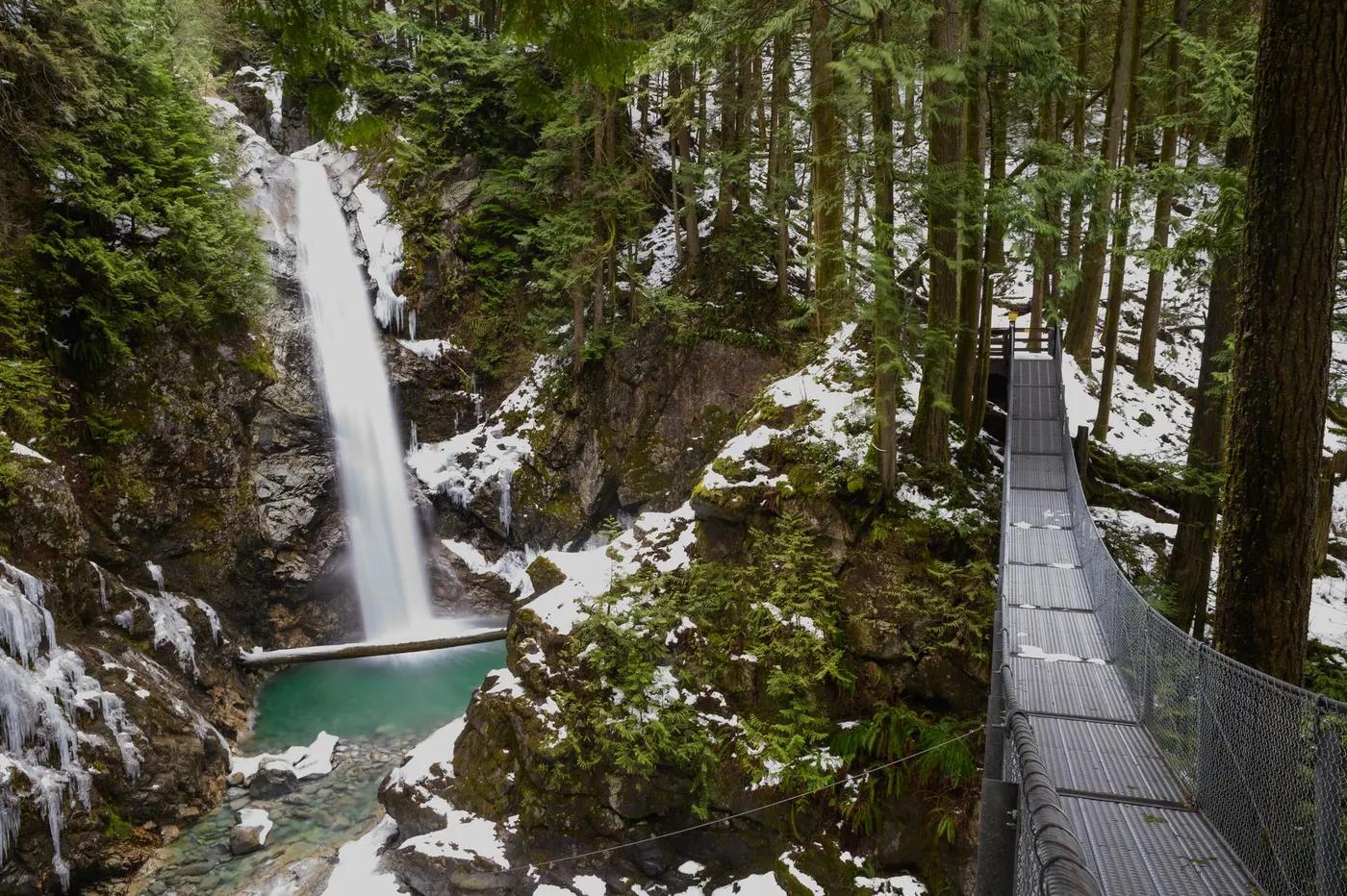 Snowy waterfall with suspension bridge in lush Mission forest.
