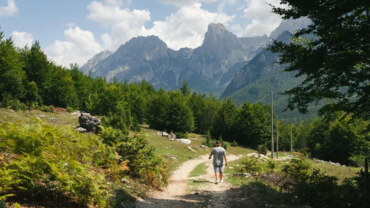 A lone hiker traversing a scenic trail in the Valbonë Valley, Albania's majestic mountains.