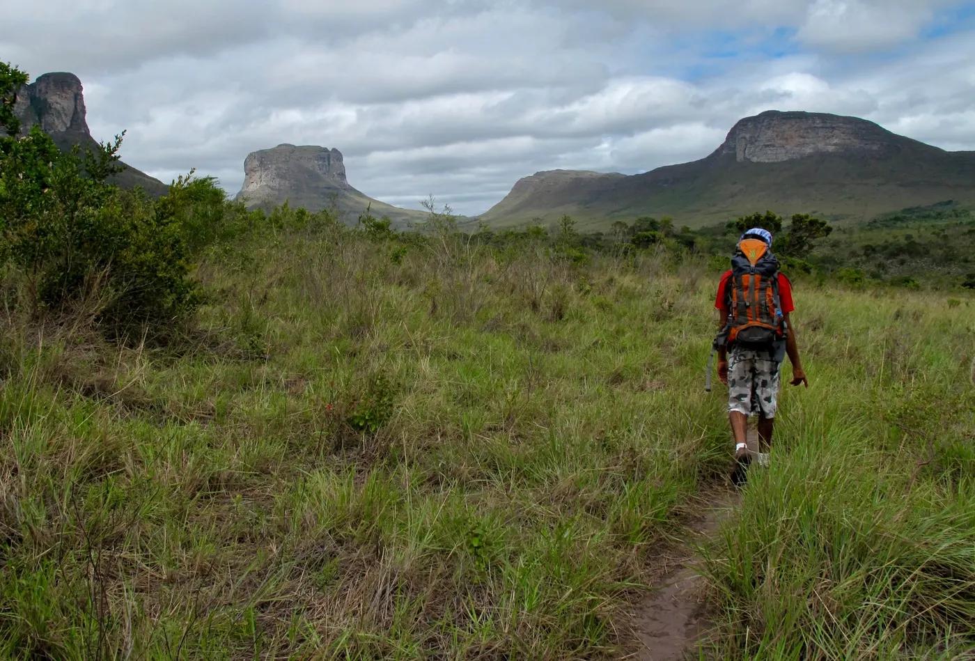 A lone hiker traverses the lush landscape of Chapada Diamantina, Brazil, under a cloudy sky.