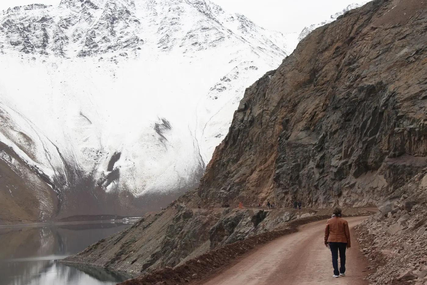 A lone hiker walks along a mountain path near a snowy peak in Yerbas Buenas, Chile.