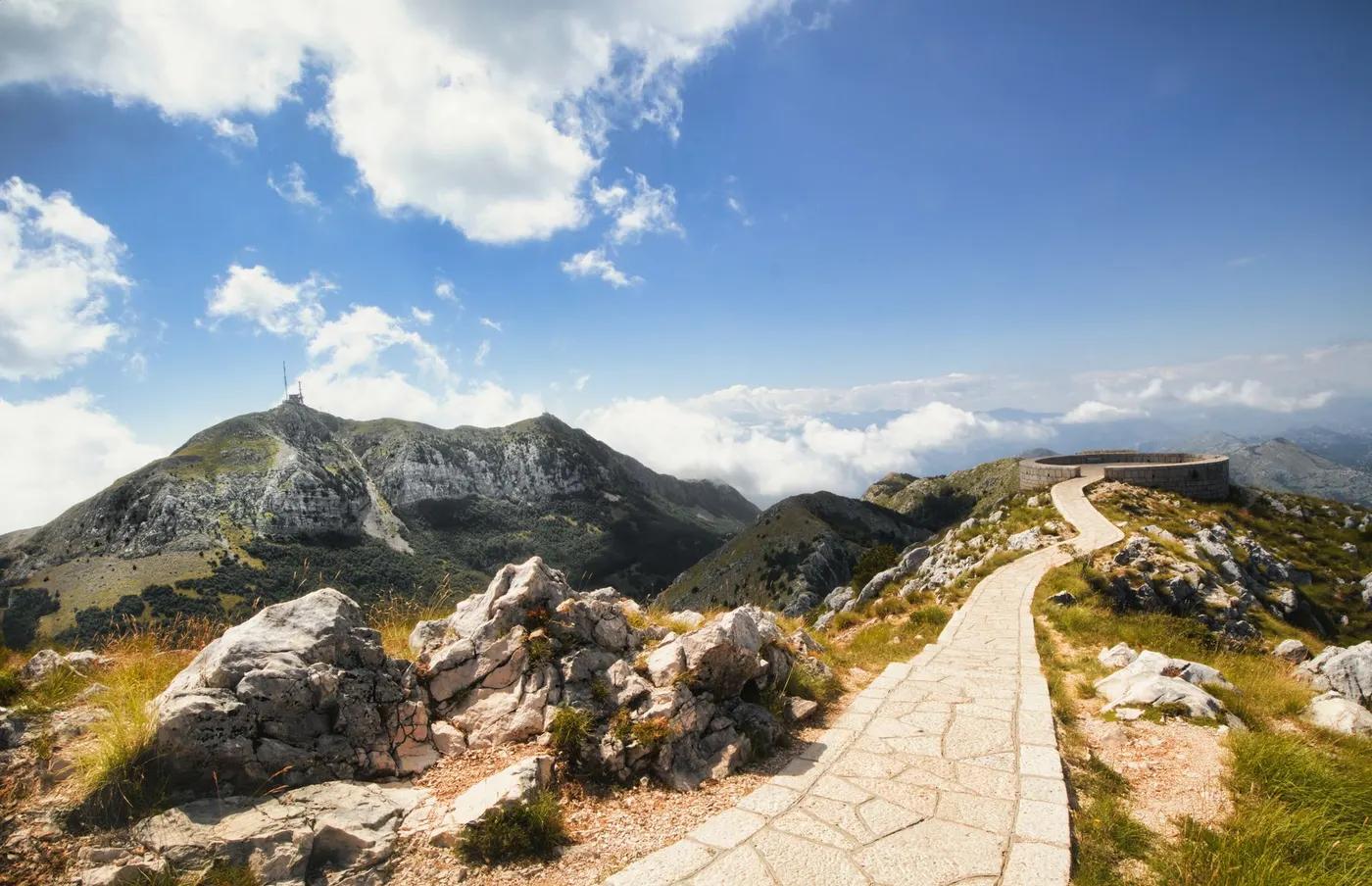 Breathtaking view of a mountain path winding through rocky terrain towards snow-capped peaks under a blue sky.