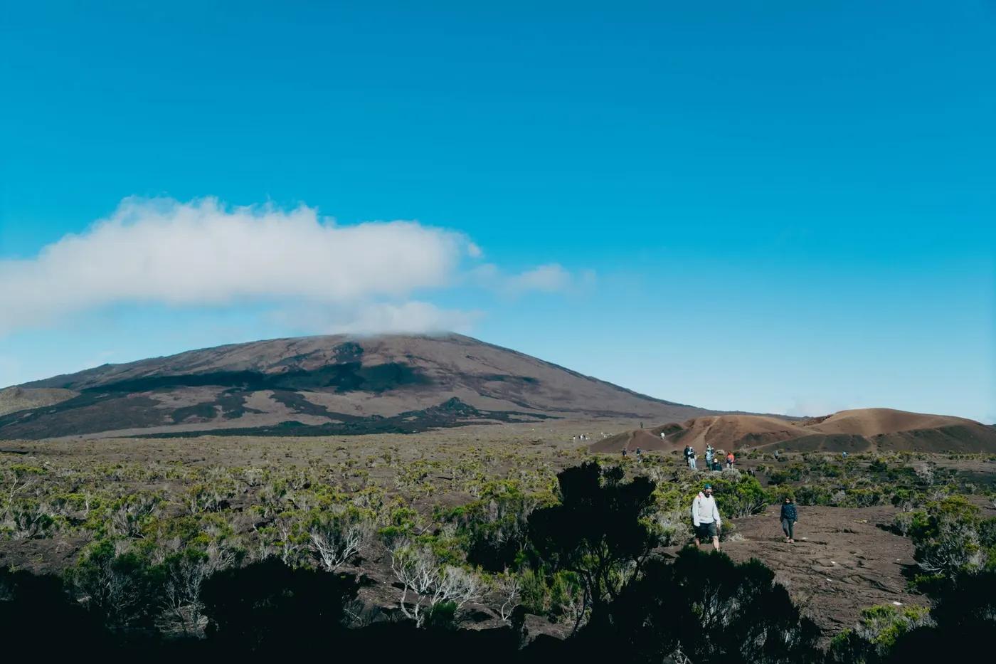 Adventurers hiking on the slopes of a volcanic landscape under a clear blue sky in La Réunion.