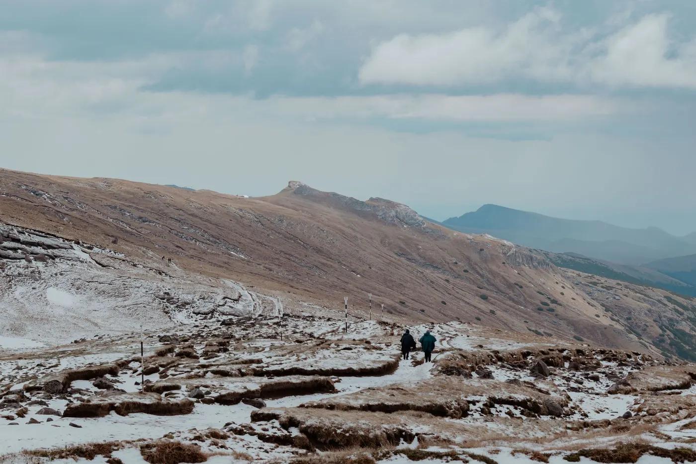 Hikers traverse a snowy trail in the scenic Bucegi Mountains, Romania.