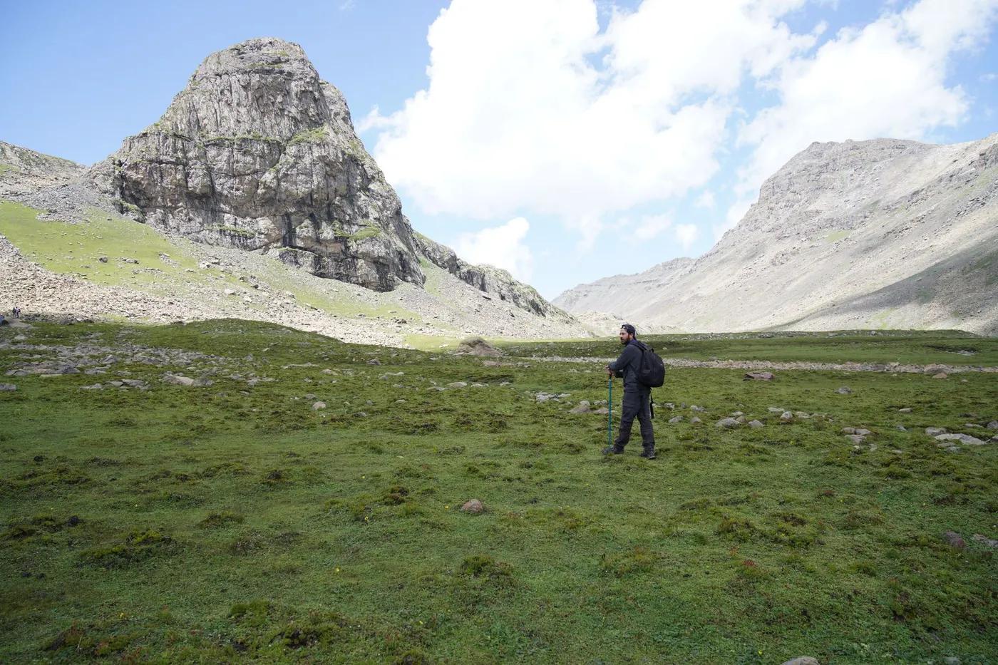 A man hiking in a vast mountain landscape with a rocky peak, capturing the essence of adventure and solitude.