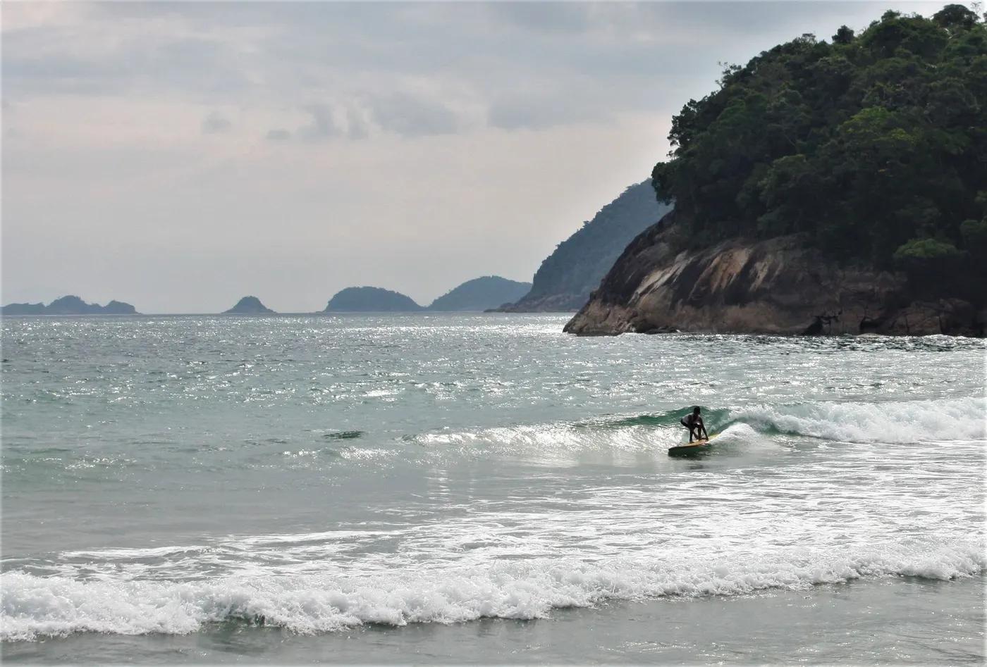 A lone surfer catches a wave on a beautiful beach with rocky landscapes in the background.