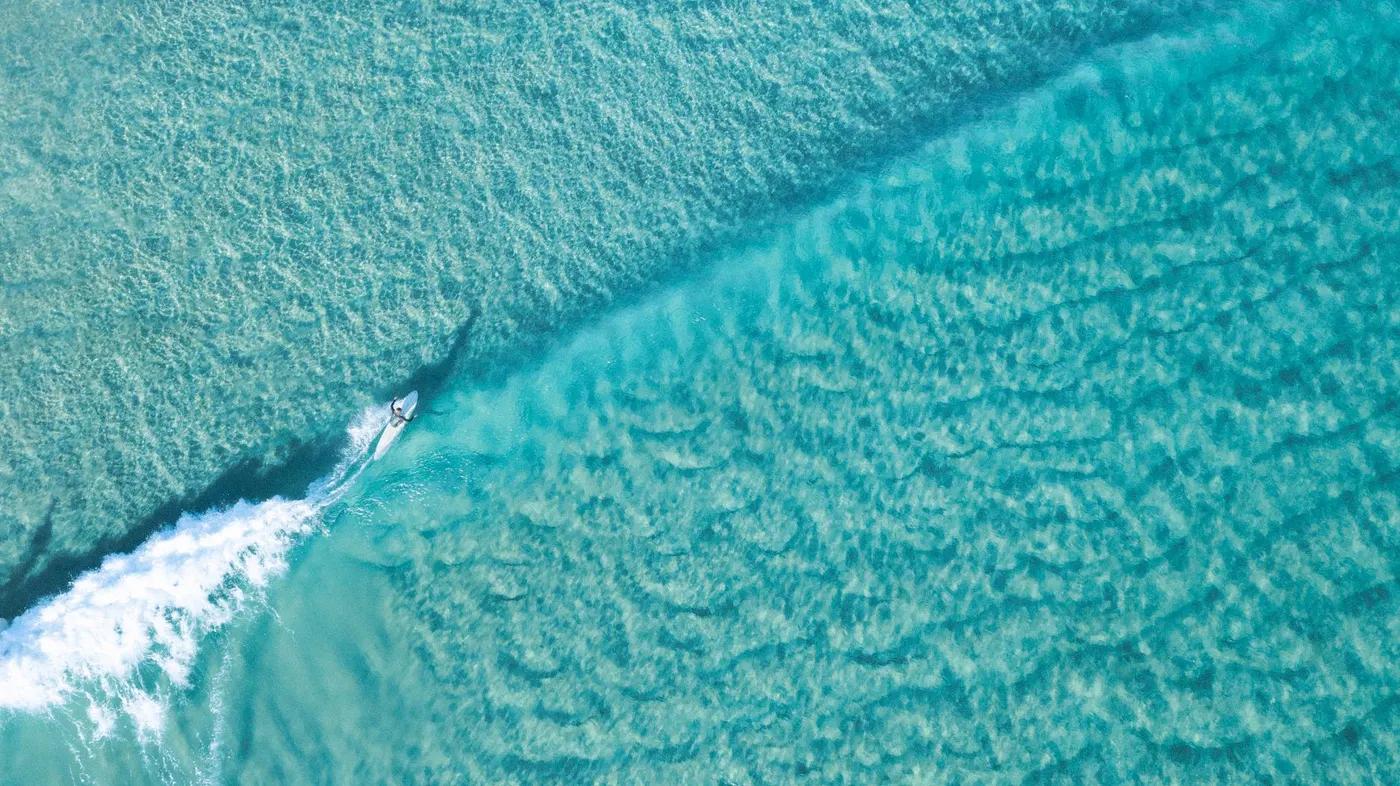 Dynamic aerial shot of a surfer riding waves in turquoise waters at Byron Bay.