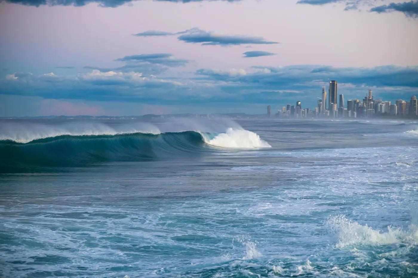 A tranquil coastal scene with waves and a distant city skyline under a colorful sky.