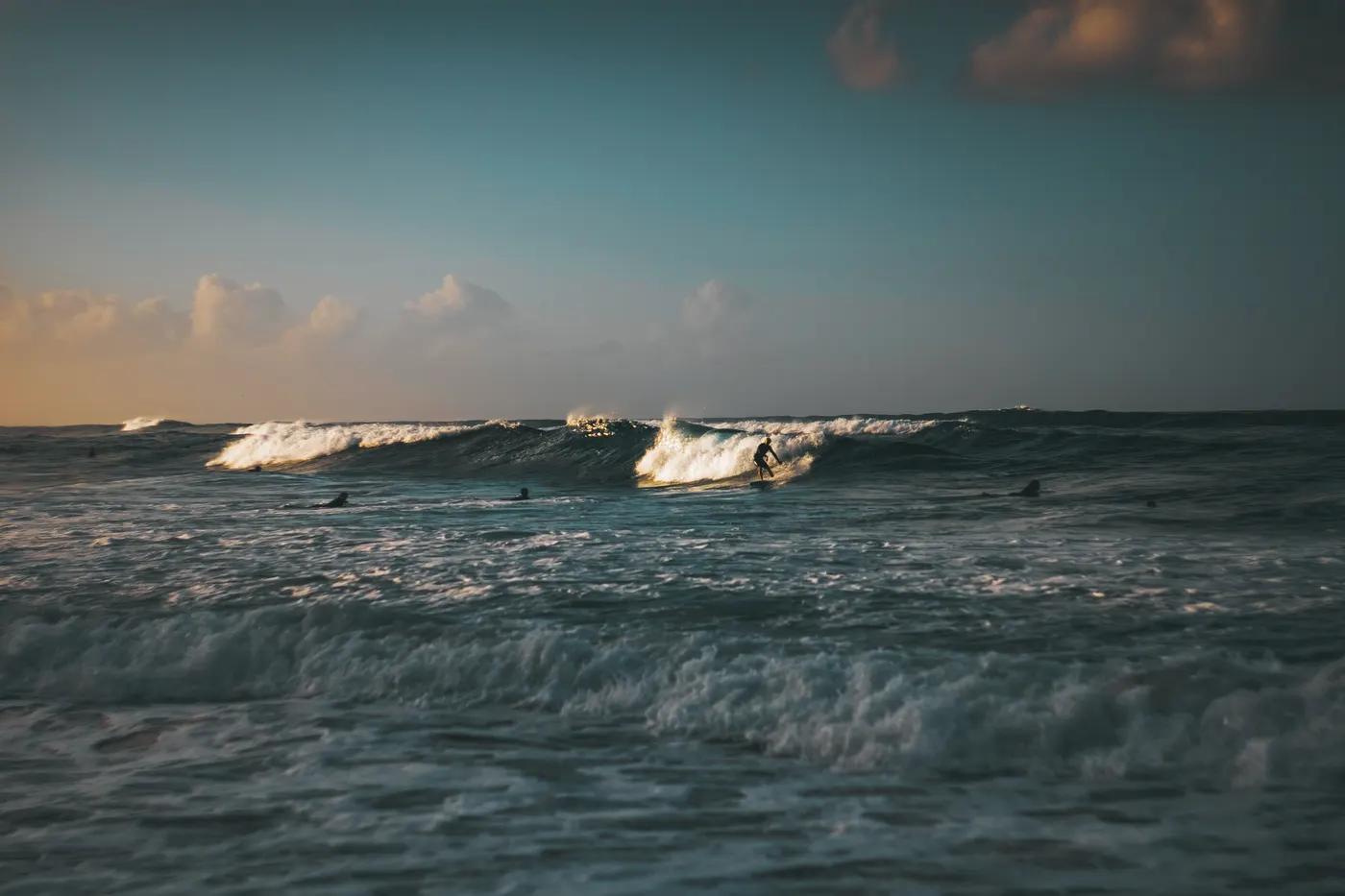 A serene beach scene with surfers braving the waves at Burleigh Heads, Queensland, during sunset.