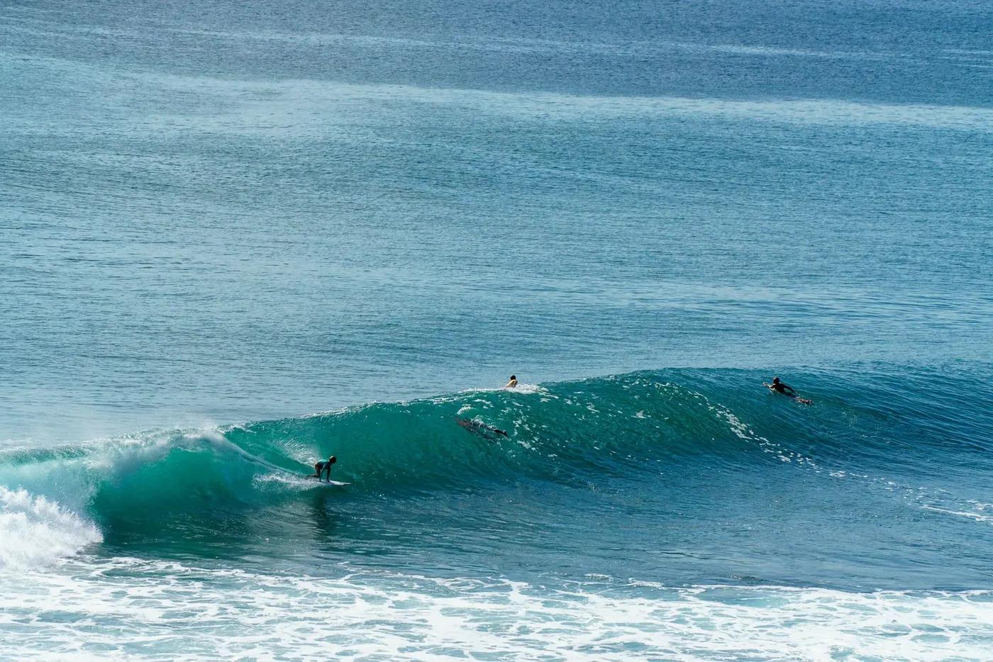 Three surfers navigating ocean waves in Bali, showcasing thrilling surf action.