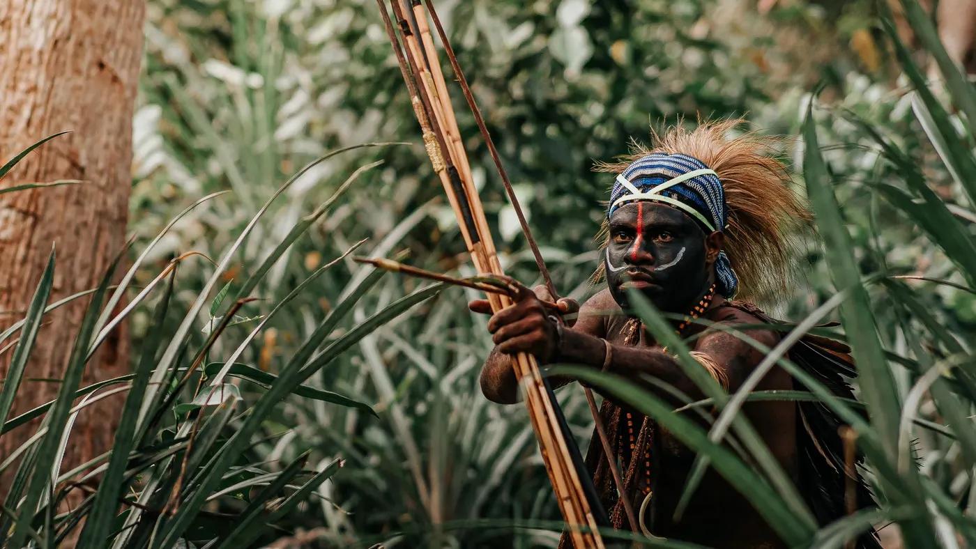 Tribal warrior with body paint and bow in Jayapura's lush jungle.