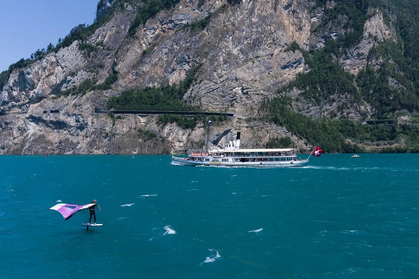 Wingsurfer gliding on Lake Lucerne with Swiss Alps backdrop and ferry in view.