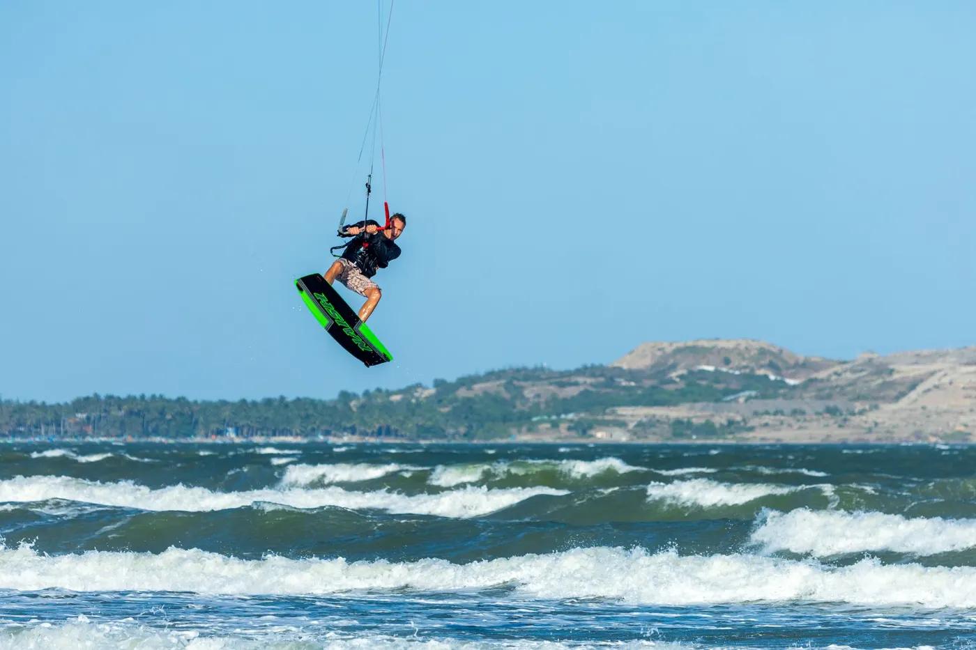 Man performing an impressive kite surfing jump over ocean waves, showcasing the thrill of outdoor water sports.