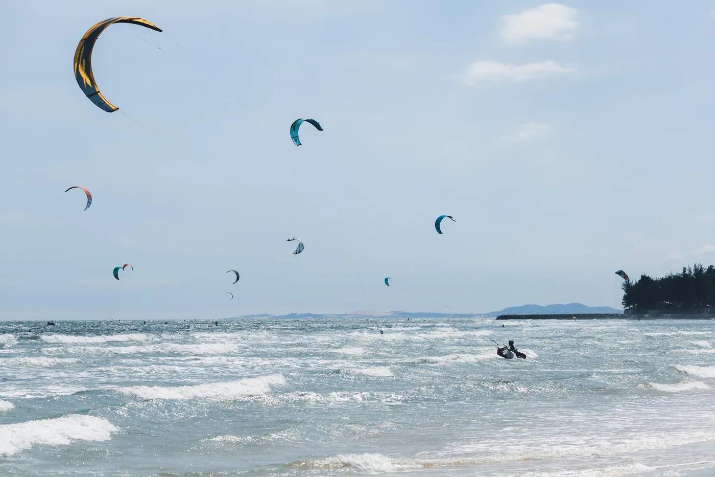 A dynamic scene of kitesurfers riding waves along a sunny coastal shore with clear skies.
