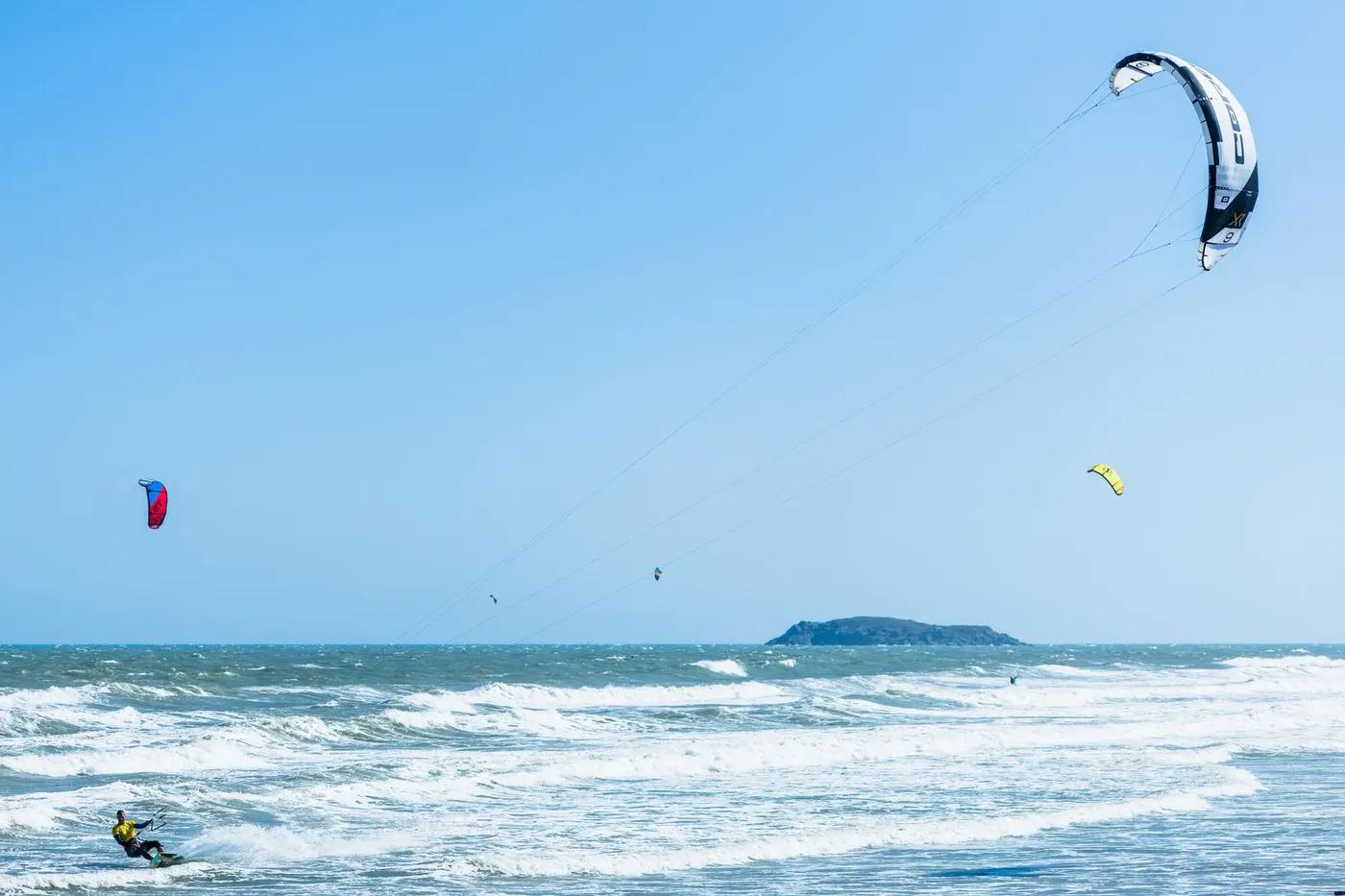 Dynamic kitesurfing action with a clear blue sky and ocean waves, perfect for adventure travel enthusiasts.