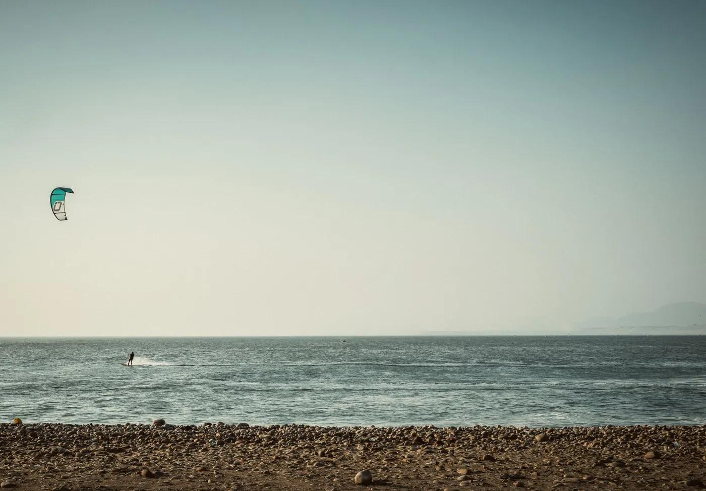 A lone kitesurfer glides over the ocean near a rocky beach in Pacasmayo, Peru.